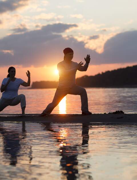 Mann und Frau zun Tai Chi bein Sonnenuntergang am Strand  | © gettyimages.com/Ulza