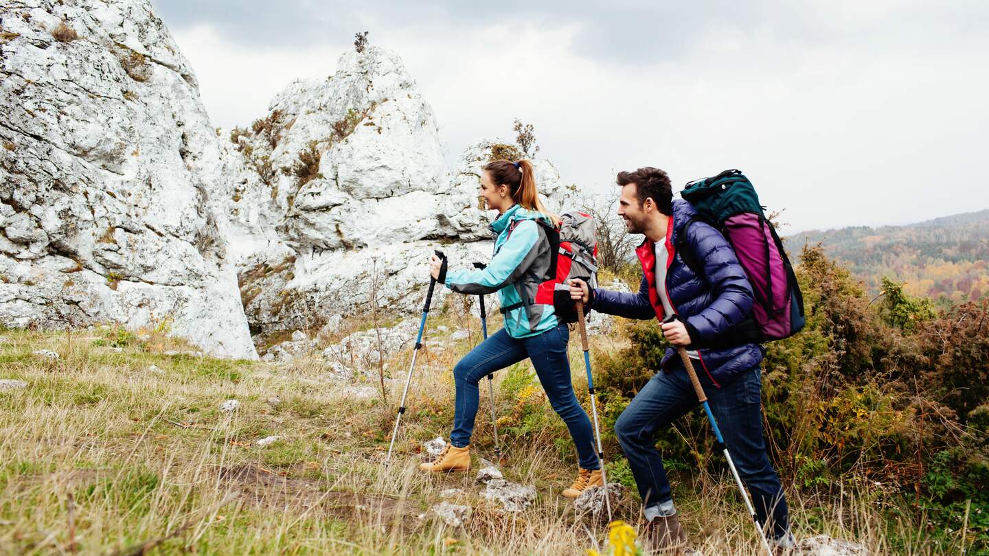 glückliches Paar mit Rucksack beim Bergwandern mit Felsen im Hintergrund | © Gettyimages.com/BartekSzewczyk