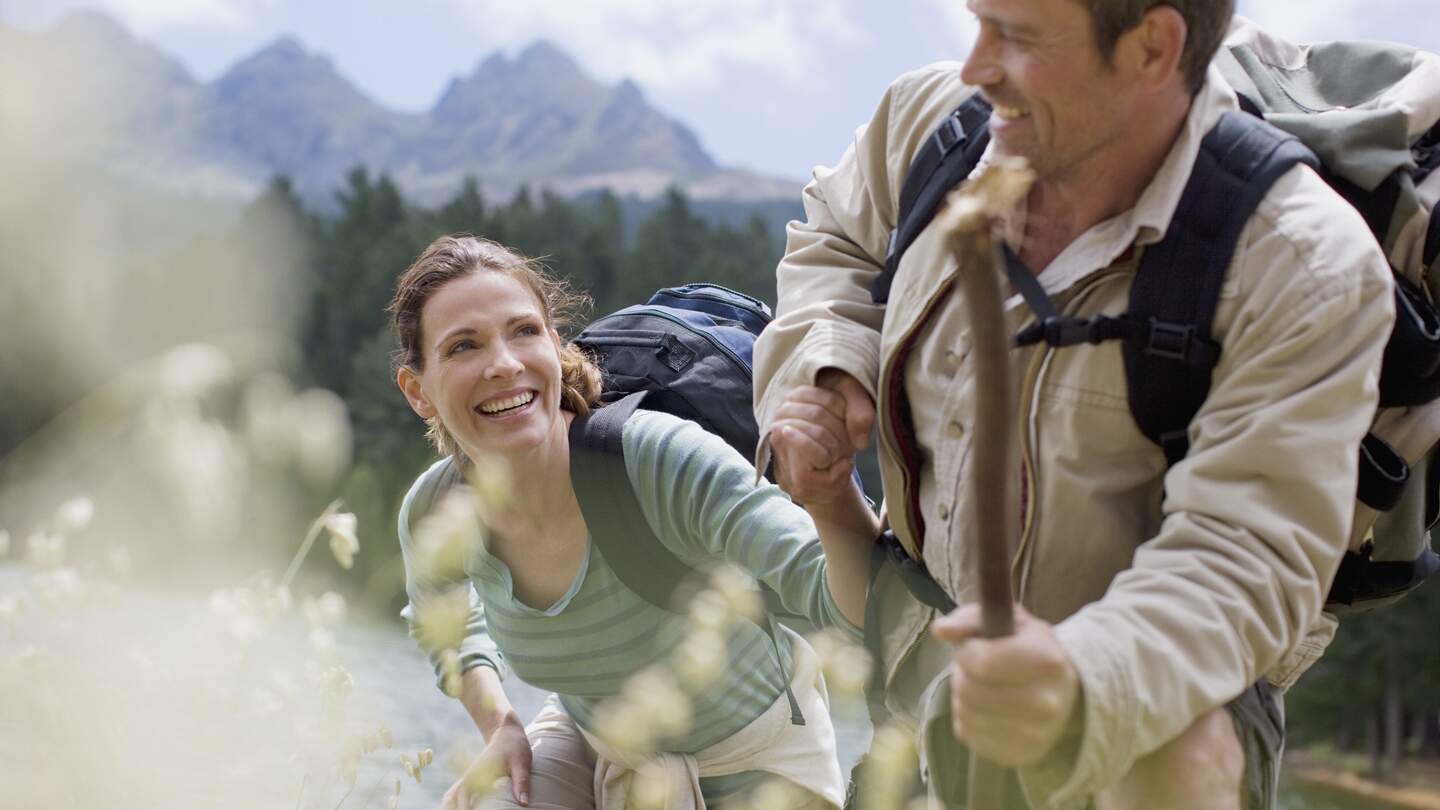 Ein Paar, das beim Wandern in einer bergigen Gegend unterwegs ist, wobei der Mann der Frau hilft. | © Gettyimages.com/Sam Edwards