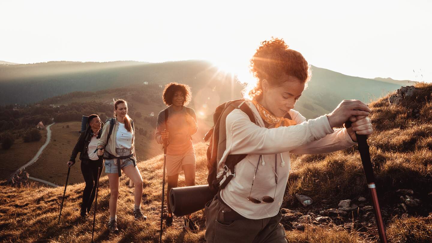 Vier Wanderer sind auf einem Bergpfad unterwegs, waehrend die Sonne tief am Horizont steht  | © gettyimages.com/Geber86