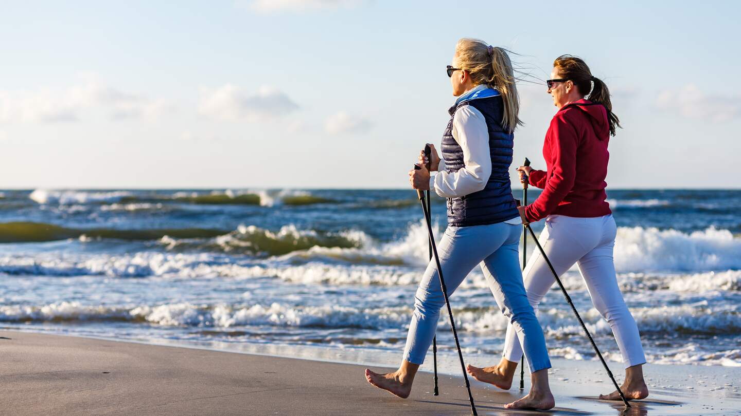 Zwei Frauen machen Nordic Walking am Strand an der Ostsee mit Brandung im Hintergrund bei Sonnenschein | © Gettyimages.com/gbh007
