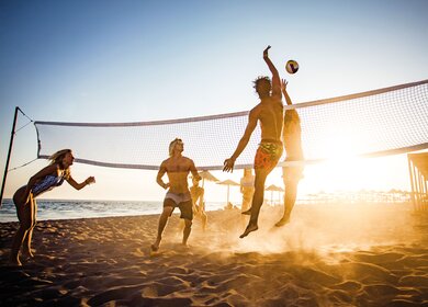Grosse Gruppe von Freunden, die am Strand Volleyball spielen | © Gettyimages.com/skynesher