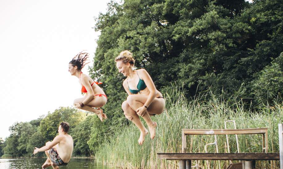 Drei junge Menschen springen in See  | © Gettyimages.com/fotografixx