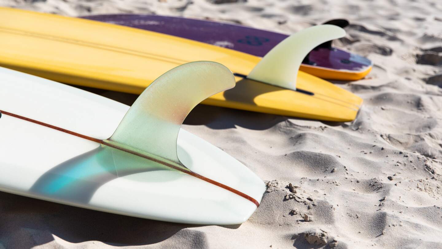 Drei Longboards liegen auf dem Sand | © Gettyimages.com/Louise Beaumont