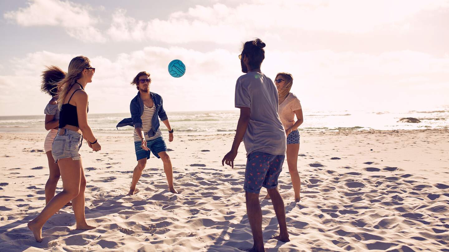  einer Gruppe gluecklicher Freunde, die Spass am Strand haben und an einem Sommertag mit Ball spielen | © Gettyimages.com/jacoblund