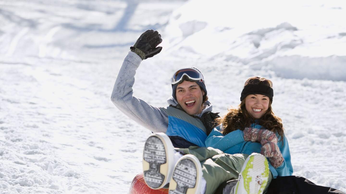Zwei Personen rodeln einen verschneiten Huegel hinunter. | © gettyimages.com/image source
