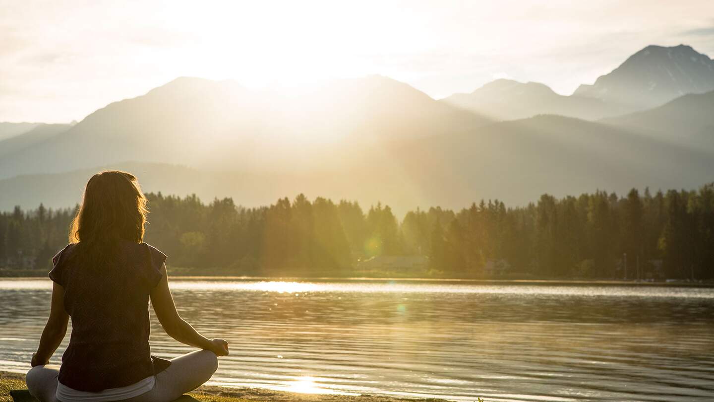 Meditation und Yogapraxis am See bei Sonnenuntergang  | © gettyimages.com/VisualCommunications