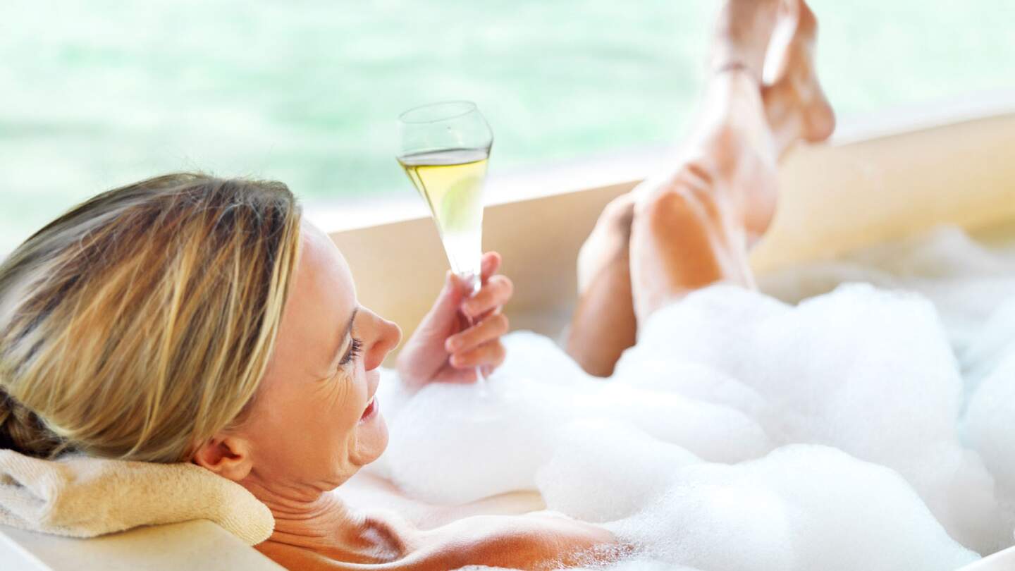 Nahaufnahme einer reifen Dame mit einem Glas Champagner in einem Schaumbad | © Gettyimages.com/Jacob Wackerhausen