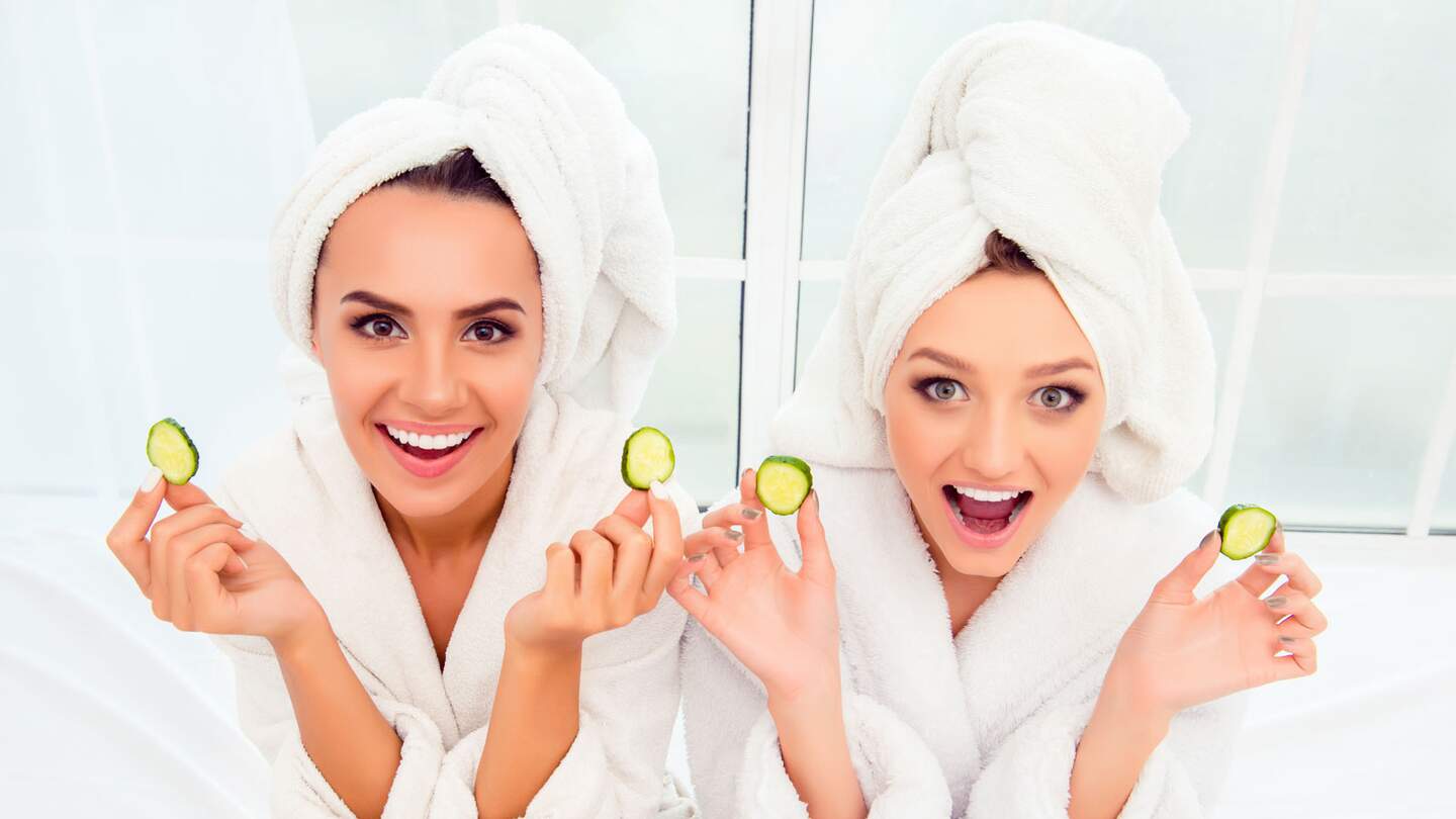 Fröhlich lächelnde Frauen in Bademänteln halten Gurkenscheiben hoch | © Gettyimages.com/Deagreez