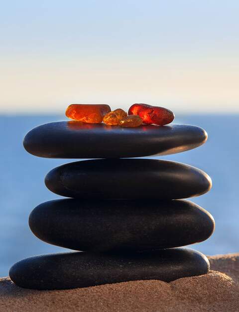 Bernstein liegt auf flachen Kieselsteinen am Meeresufer in den Strahlen der untergehenden Sonne | © Gettyimages.com/ires007