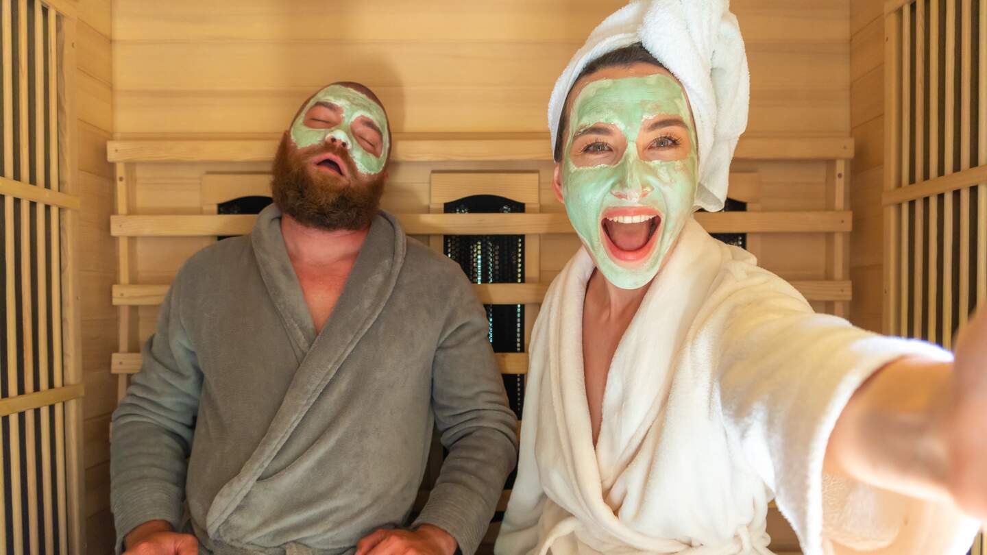 Ein junges lustiges Paar mit entspannen SPA Tag in der Sauna, eine Frau macht Selfie mit Schoenheitsmaske, während ihr Freund schlaeft | © Gettyimages.com/Alina Rosanova