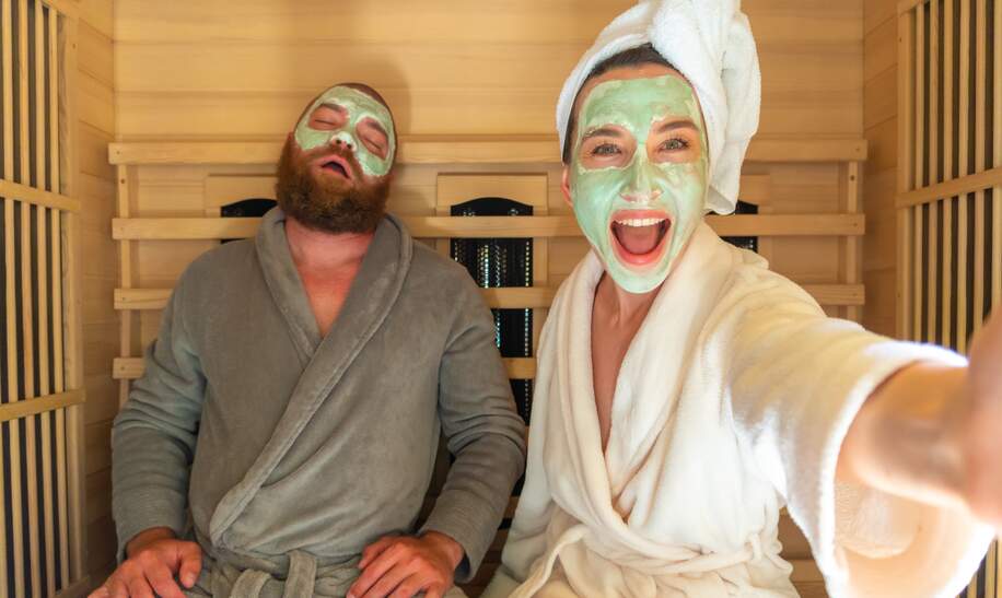 Ein junges lustiges Paar mit entspannen SPA Tag in der Sauna, eine Frau macht Selfie mit Schoenheitsmaske, während ihr Freund schlaeft | © Gettyimages.com/Alina Rosanova