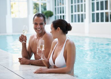 Beschnittene Aufnahme eines liebevollen Paares, das Champagner trinkt, waehrend es sich in einem Pool entspannt | © Gettyimages.com/PeopleImages