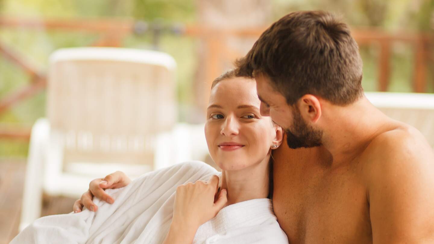 Liebevolles junges Paar, das auf seinem Wochenendausflug auf einem Liegestuhl im Spa-Resort kuschelt | © Gettyimages.com/fotostorm