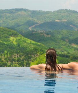 Rueckansicht des Paares mit Blick auf die Berglandschaft vom Infinity-Pool aus | © Gettyimages.com/Soft_Light