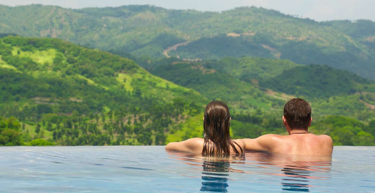 Rueckansicht des Paares mit Blick auf die Berglandschaft vom Infinity-Pool aus | © Gettyimages.com/Soft_Light