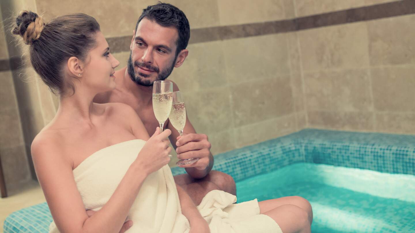 Junges Paar entspannt sich im Pool mit einem Glas Sekt | © Gettyimages.com/ZoneCreative