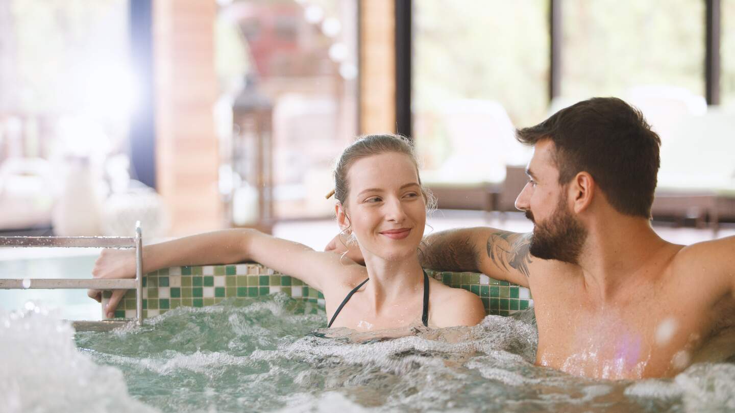 Glueckliches Paar sitzt in einem Whirlpool im Spa-Resort | © Gettyimages.com/fotostorm