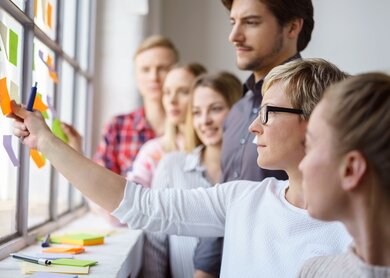 Junges Team von fokussierten Berufseinsteigern, die Ideen diskutieren und mit Haftnotizen an einem Buerofenster brainstormen | © Gettyimages.com/stockfour