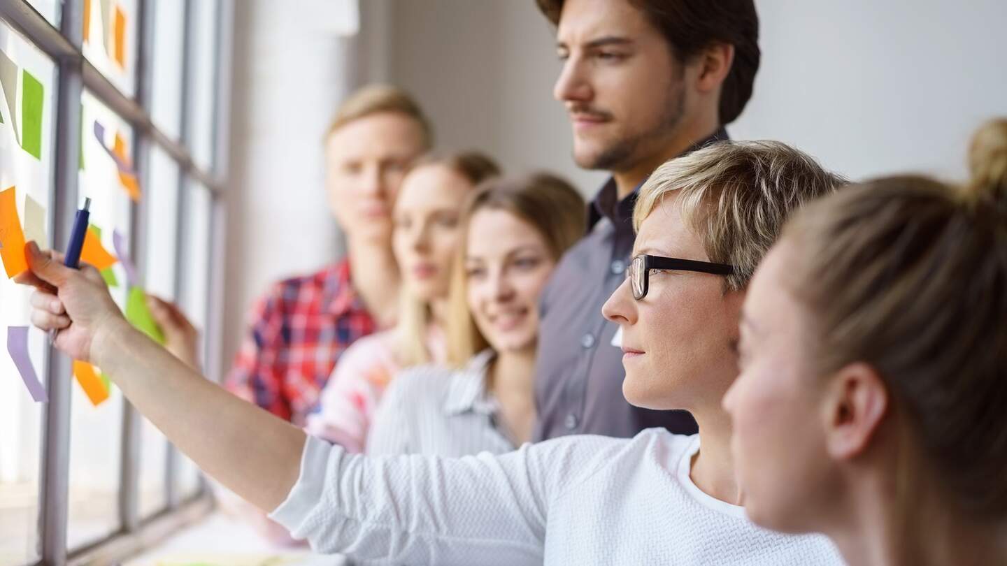 Junges Team von fokussierten Berufseinsteigern, die Ideen diskutieren und mit Haftnotizen an einem Buerofenster brainstormen | © Gettyimages.com/stockfour