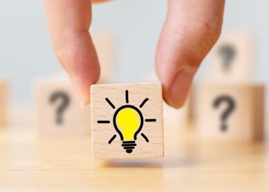 Handverlesener Holzwuerfel mit Fragezeichen Symbol und Gluehbirnensymbol | © Gettyimages.com/marchmeena29