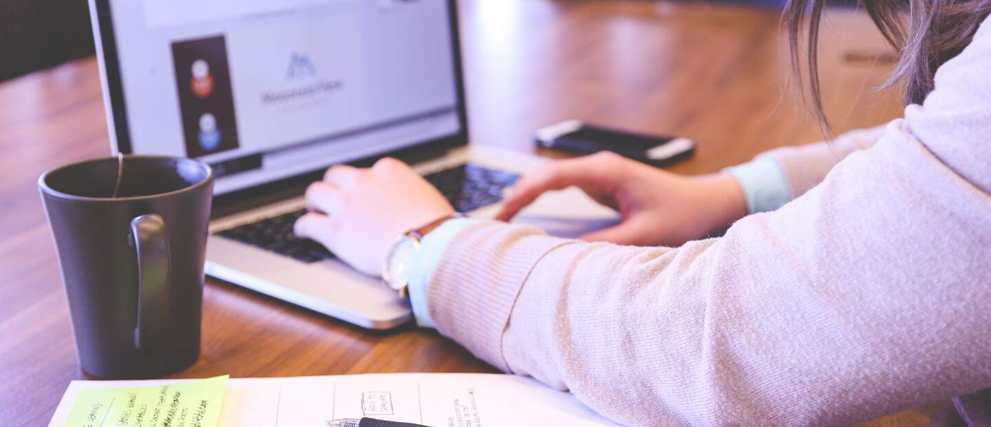Angeschnittene Frau, die auf einem geoeffneten Laptop tippt, waehrend neben ihr liegt ein Blatt mit Notizen und eine Teetasse | © Pixabay/StartupStockPhotos 