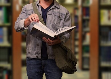 Angeschnittener Mann steht zwischen Buecherregalen und blaettert in einem Buch | © Pixabay/geralt