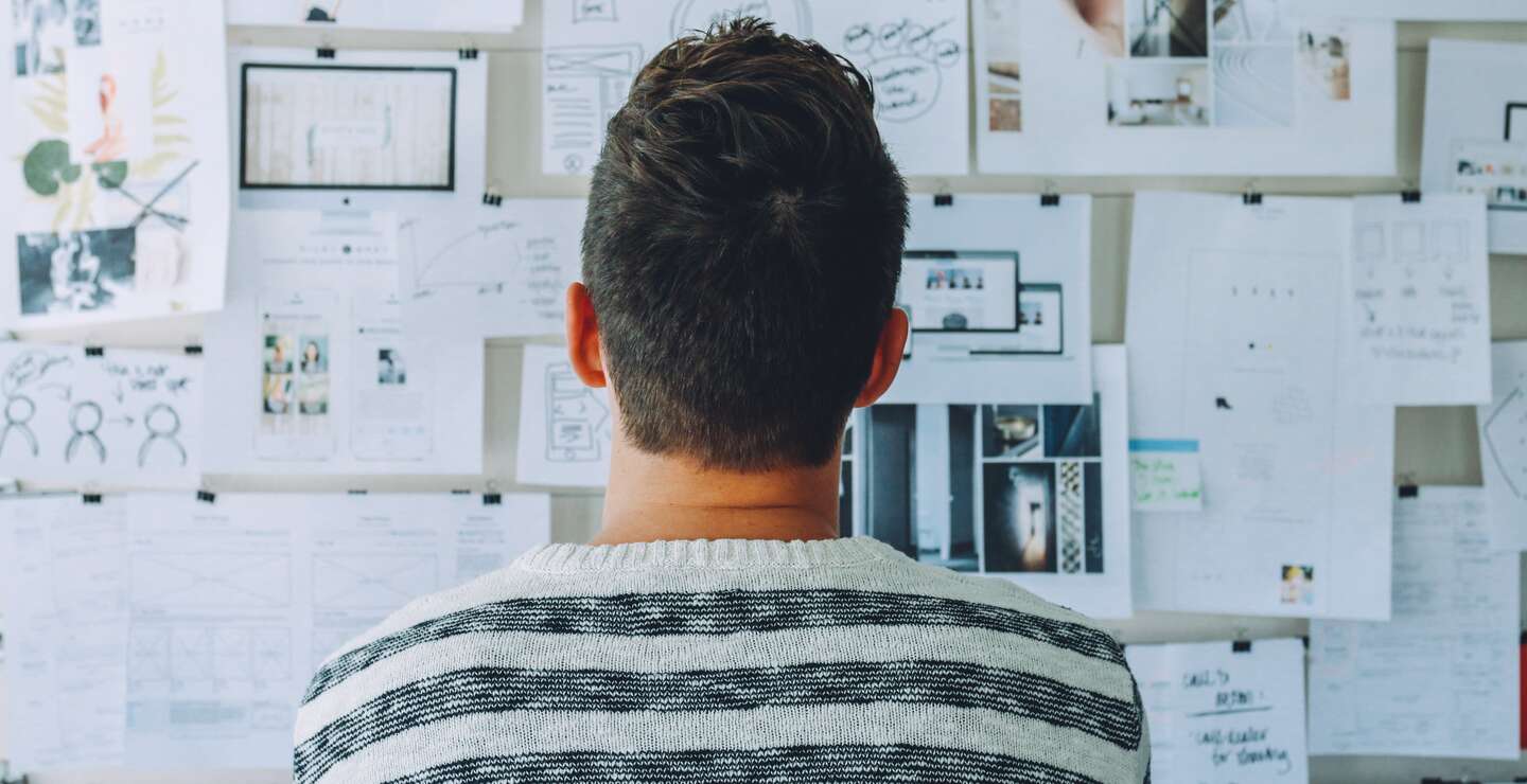 Mann von hinten steht vor einer Wand mit einer Collage aus Notizen, Bildern und Skizzen, die ihm bei der Planung helfen | © Pixabay/Pexels
