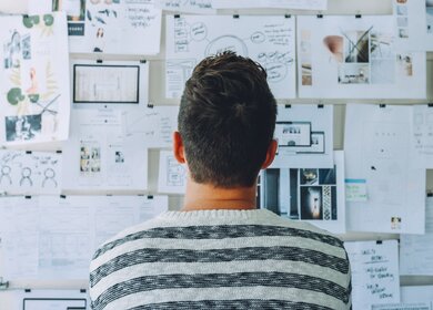 Mann von hinten steht vor einer Wand mit einer Collage aus Notizen, Bildern und Skizzen, die ihm bei der Planung helfen | © Pixabay/Pexels