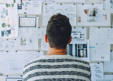 Mann von hinten steht vor einer Wand mit einer Collage aus Notizen, Bildern und Skizzen, die ihm bei der Planung helfen | © Pixabay/Pexels