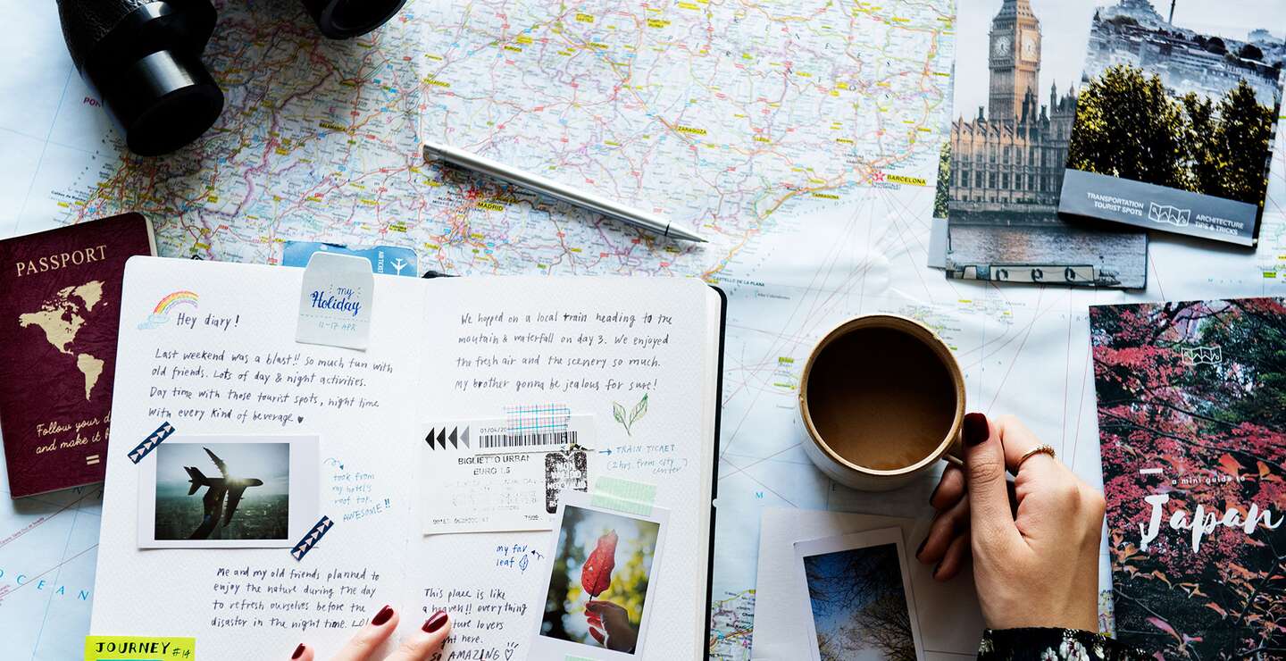 eine flache Anordnung verschiedener Reiseutensilien auf einer Oberflaeche, darunter eine Karte, ein Fernglas, ein Reisepass, Postkarten, Fotos und eine Tasse Kaffee | © gettyimages.com/Rawpixel Ltd.