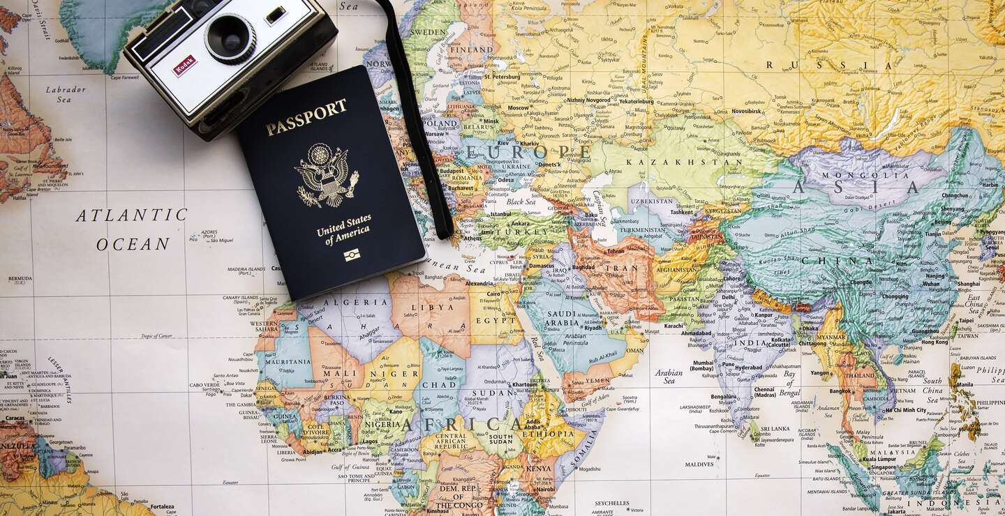 Auf einer bunten Weltkarte liegen ein altmodischer Fotapparat und ein Reisepass | © Pixabay/Pamjpat